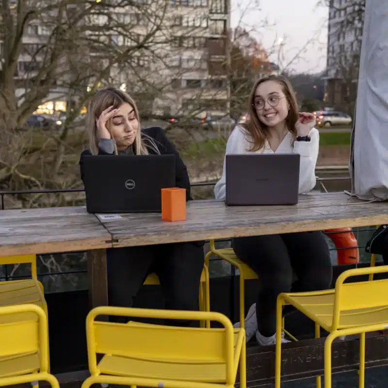 Deux jeunes femmes avec ordinateurs portables assises à une table en plein air à Lille.