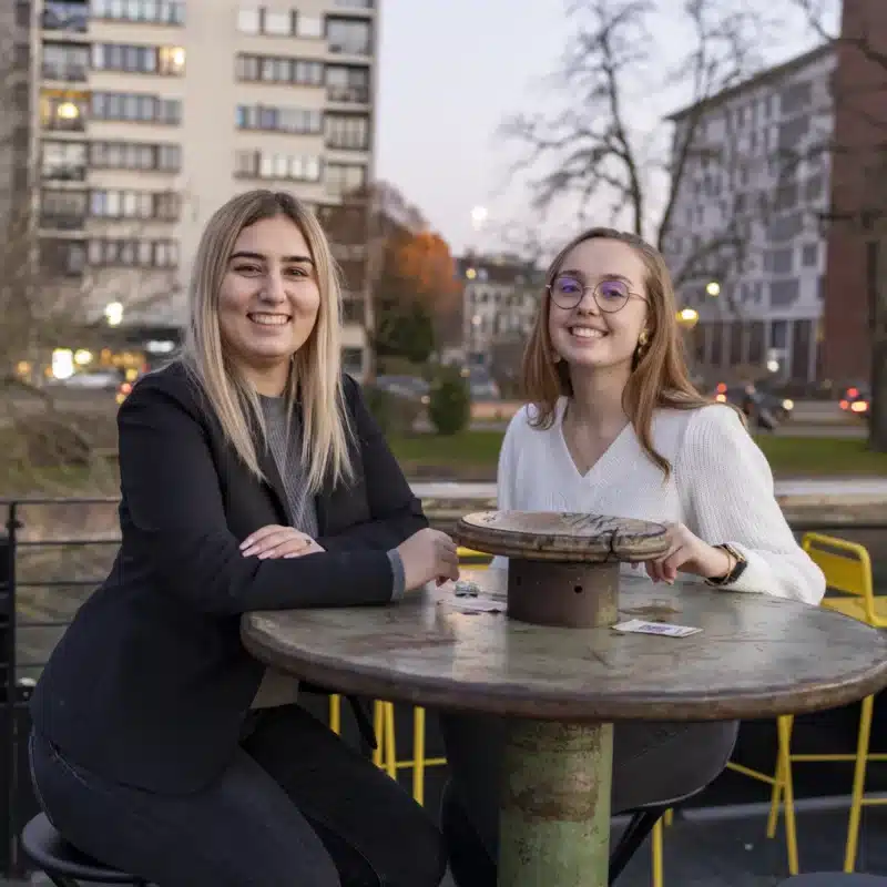 Photo de deux jeunes femmes souriantes assises à une table en extérieur dans un parc urbain à Lil.