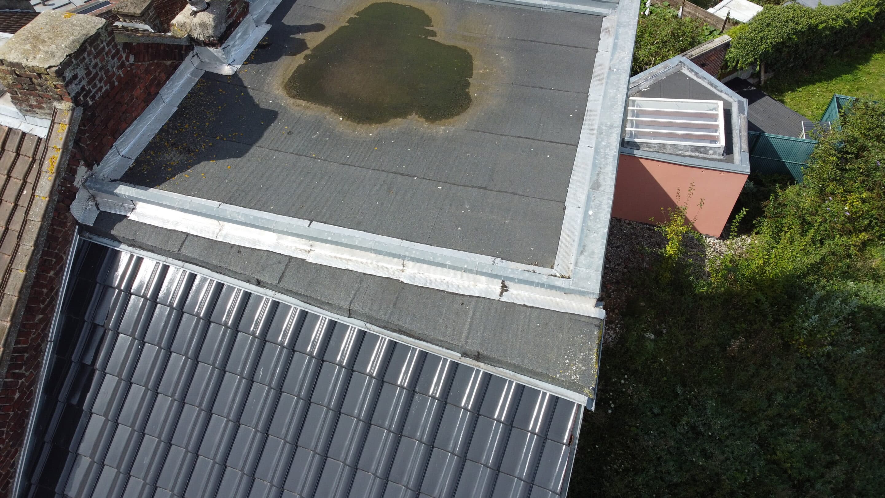 Toit avec zone endommagée et jardin verdoyant en arrière-plan.