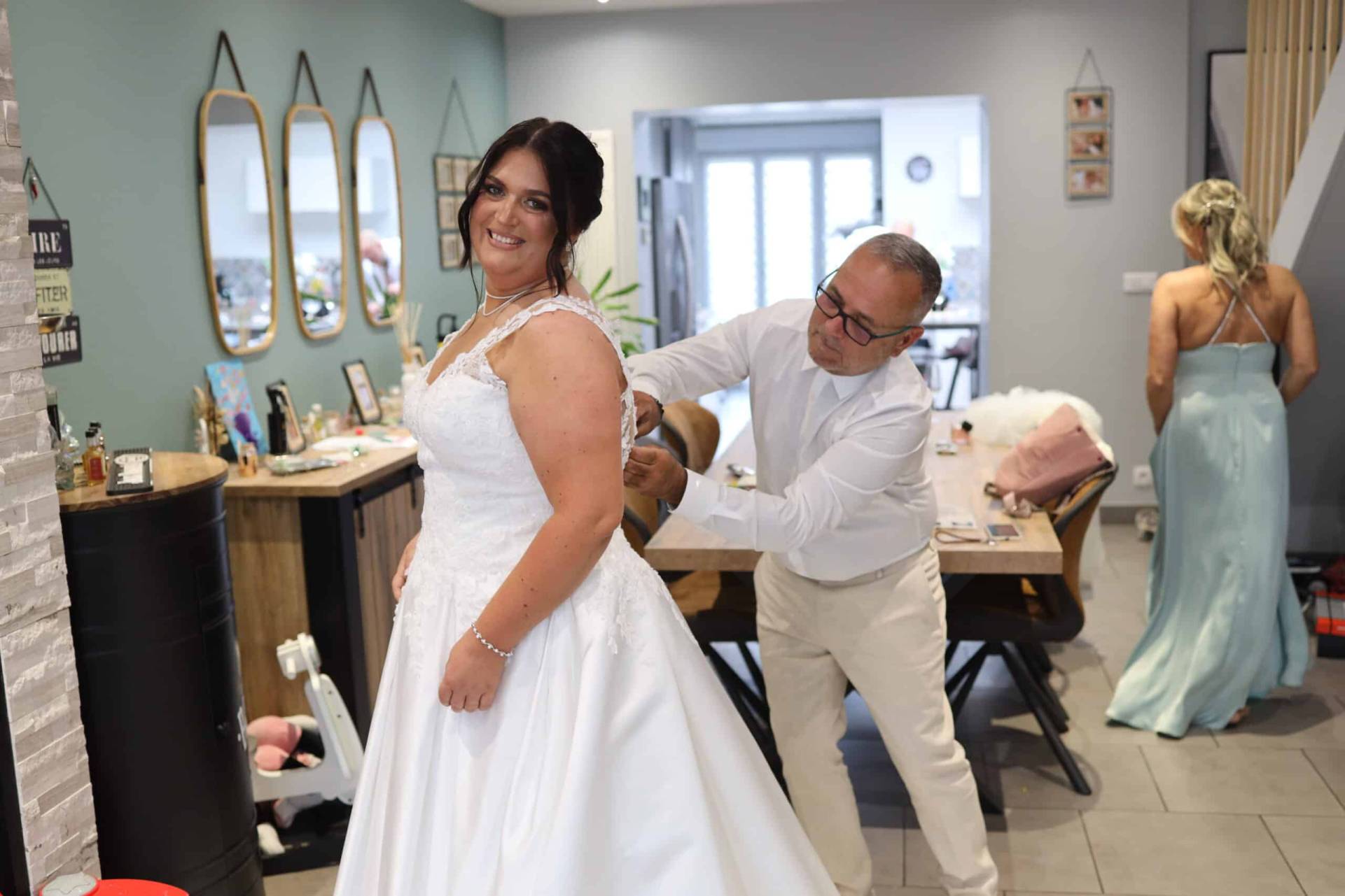 Vendeuse en robe de mariée aidant une mariée à s'habiller dans une boutique de mariage à Lille.