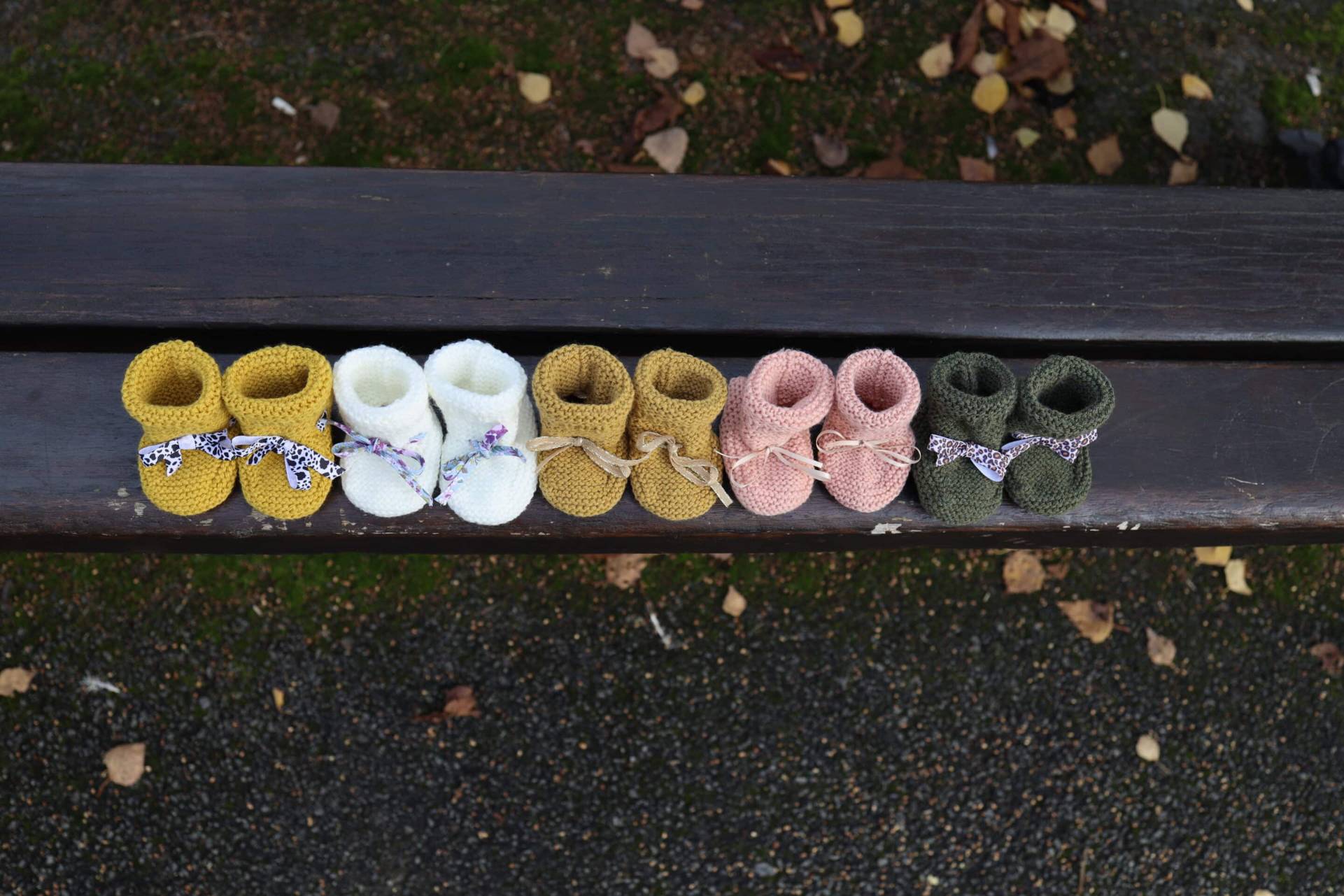 Chaussures bébé tricotées en différentes couleurs, posées sur un banc en bois.